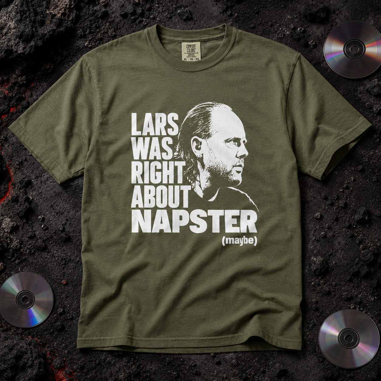 An olive green graphic t-shirt laid flat on a dark textured background with three CD-ROMs in the corners. The shirt features a white graphic print of Lars Ulrich's profile next to the text 'LARS WAS RIGHT ABOUT NAPSTER (maybe)'.