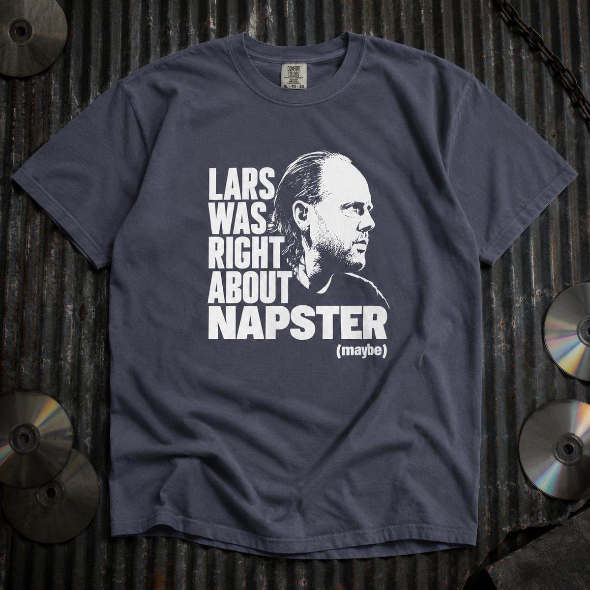 A dark slate blue graphic t-shirt laid flat on a corrugated metal background, featuring a black and white portrait of Lars Ulrich and the text 'LARS WAS RIGHT ABOUT NAPSTER (maybe)'.